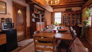 Une salle à manger en bois avec une grande table, des chaises et un lustre. On y trouve également un réfrigérateur, des placards et une fenêtre ornée de plantes.