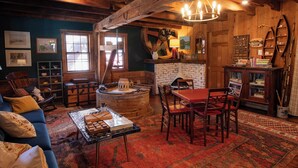 Un intérieur rustique avec un plafond en bois, un coin repas avec une table et des chaises rouges, un canapé avec des coussins et un tapis à motifs.