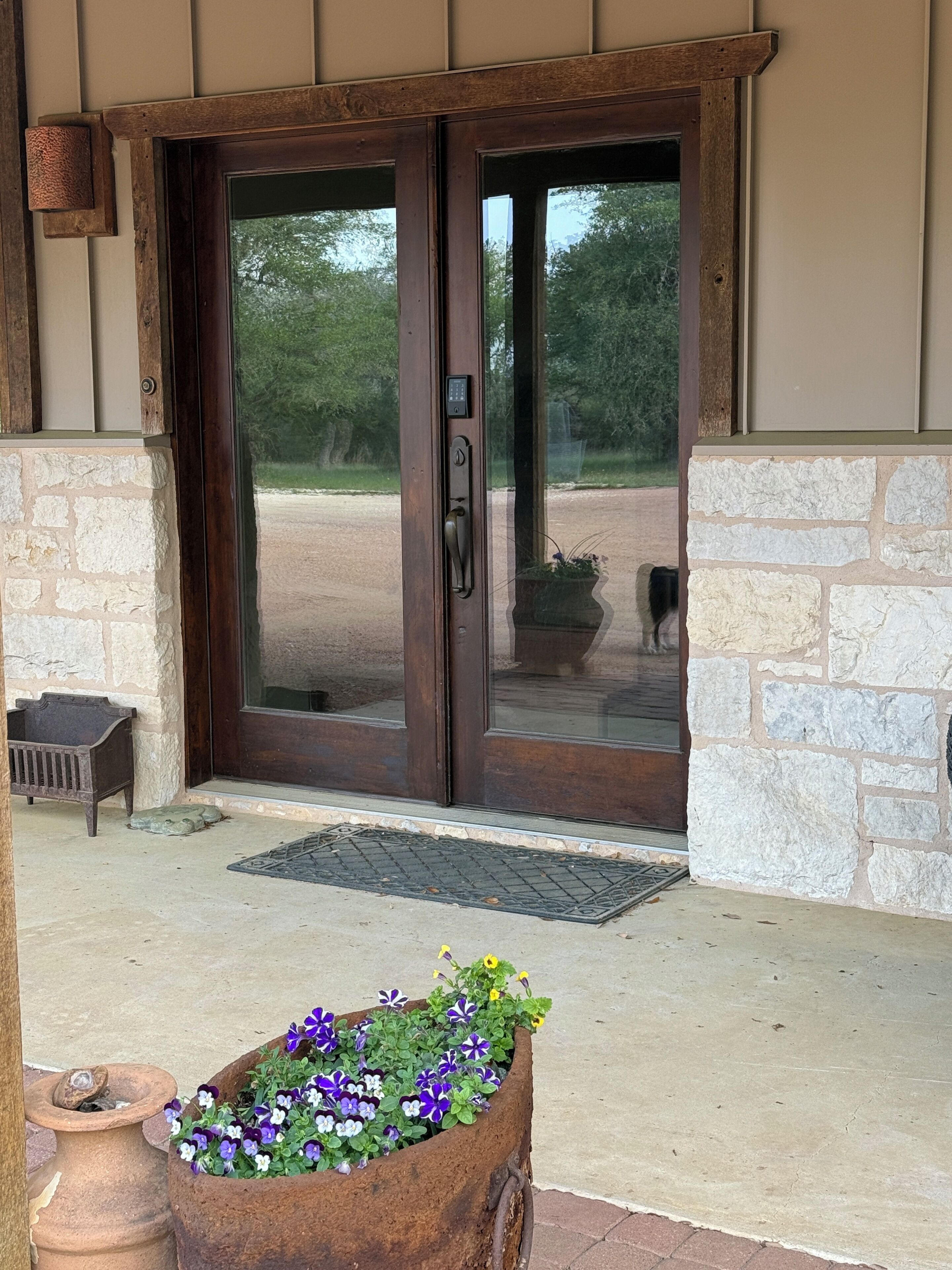 A wooden door with a keypad lock, a stone planter with flowers, and a bench outside a building.