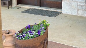 A wooden door with a keypad lock, a stone planter with flowers, and a bench outside a building. - Hill Country Escape near Wineries, Mae’s Ridge Wedding Venue & P. Falls State Pk (Johnson City)