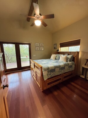 A bedroom with a wooden bed, a ceiling fan, a window with a view, and a balcony.