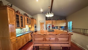 A spacious kitchen with wooden cabinets, a central island, and a hanging light fixture. - Hill Country Escape near Wineries, Mae’s Ridge Wedding Venue & P. Falls State Pk (Johnson City)