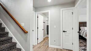 A hallway with a staircase, a shower area, and a bedroom with a bed and nightstand.
