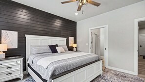 A bedroom with a bed, nightstands, a ceiling fan, and a door leading to another room.