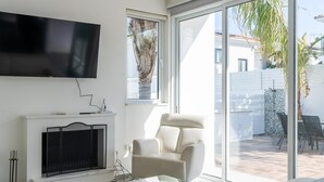 Un soggiorno moderno con una televisione a schermo piatto, un camino, un tavolino da caffè in vetro e un'ampia porta scorrevole in vetro che dà su un patio esterno.