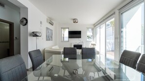 Una sala riunioni moderna con tavolo in vetro, quattro sedie, un divano, una televisione a schermo piatto e ampie finestre.