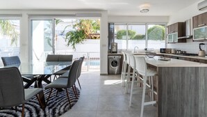Una cucina moderna con isola centrale, zona pranzo con tavolo in vetro e vista sull'esterno.