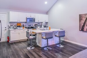 Eine moderne Küche mit weißen Schränken, einer Mikrowelle, einer Kaffeemaschine und einer Bar mit Hockern.