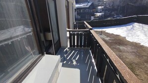 En balkon med udsigt over et sneklædt landskab og huse i baggrunden.