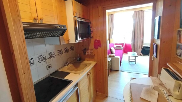 Et lille køkken med mikrobølgeovn, komfur og vask, der fører ud til en balkon med sofa og fjernsyn.