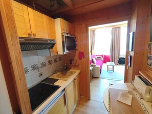 Eine kleine Küche mit Mikrowelle, Herd und Spüle, die zu einem Balkon mit Sofa und Fernseher führt.