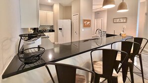 Una cocina moderna con una isla central, armarios blancos e iluminación colgante.