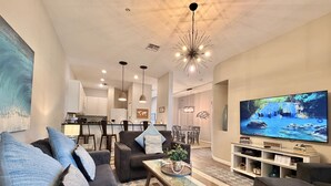 Una sala de estar moderna con un sofá, una mesa de centro, televisión y una cocina al fondo.