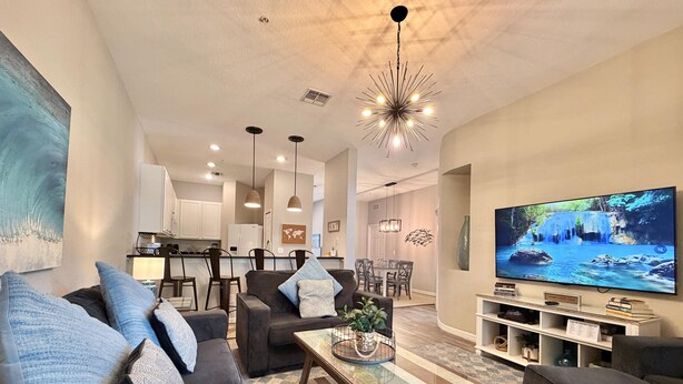 Uma sala de estar moderna com sofá, mesa de centro, TV e cozinha ao fundo.