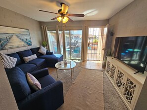 Ein Wohnzimmer mit einer Couch, einem Couchtisch, einem Deckenventilator, einem Fernseher und Blick durch eine Glastür.