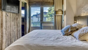 Una camera da letto con un letto, una televisione a muro, una finestra con tende e vista sull'esterno.