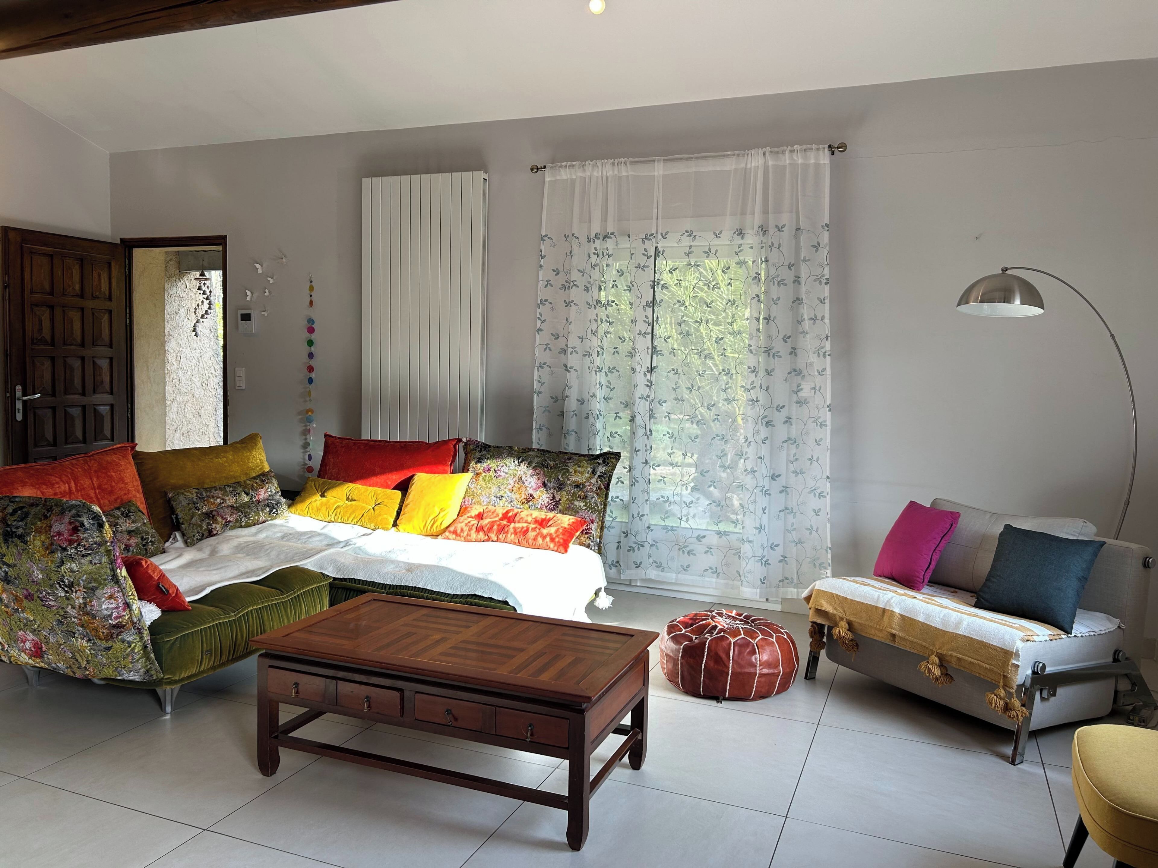 A room with a bed, sofa, ottoman, and a wooden table.