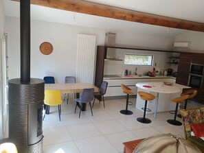 A modern kitchen with a central island, a dining area with a table and chairs, and a wood-burning stove. - House in Rochefort with Private Pool & AC (Rochefort-du-Gard)