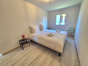 Une chambre d’hôtel avec deux lits, une petite table avec une lampe, une chaise et une fenêtre donnant sur un beau paysage.