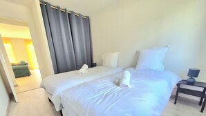 Ein Hotelzimmer mit einem großen Bett, einem Nachttisch mit Lampe und Blick auf ein weiteres Zimmer durch eine offene Tür.