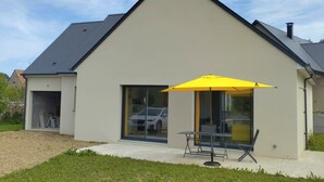 Ein modernes Haus mit einem großen Glasfenster, einem gelben Sonnenschirm und einer kleinen Terrasse.