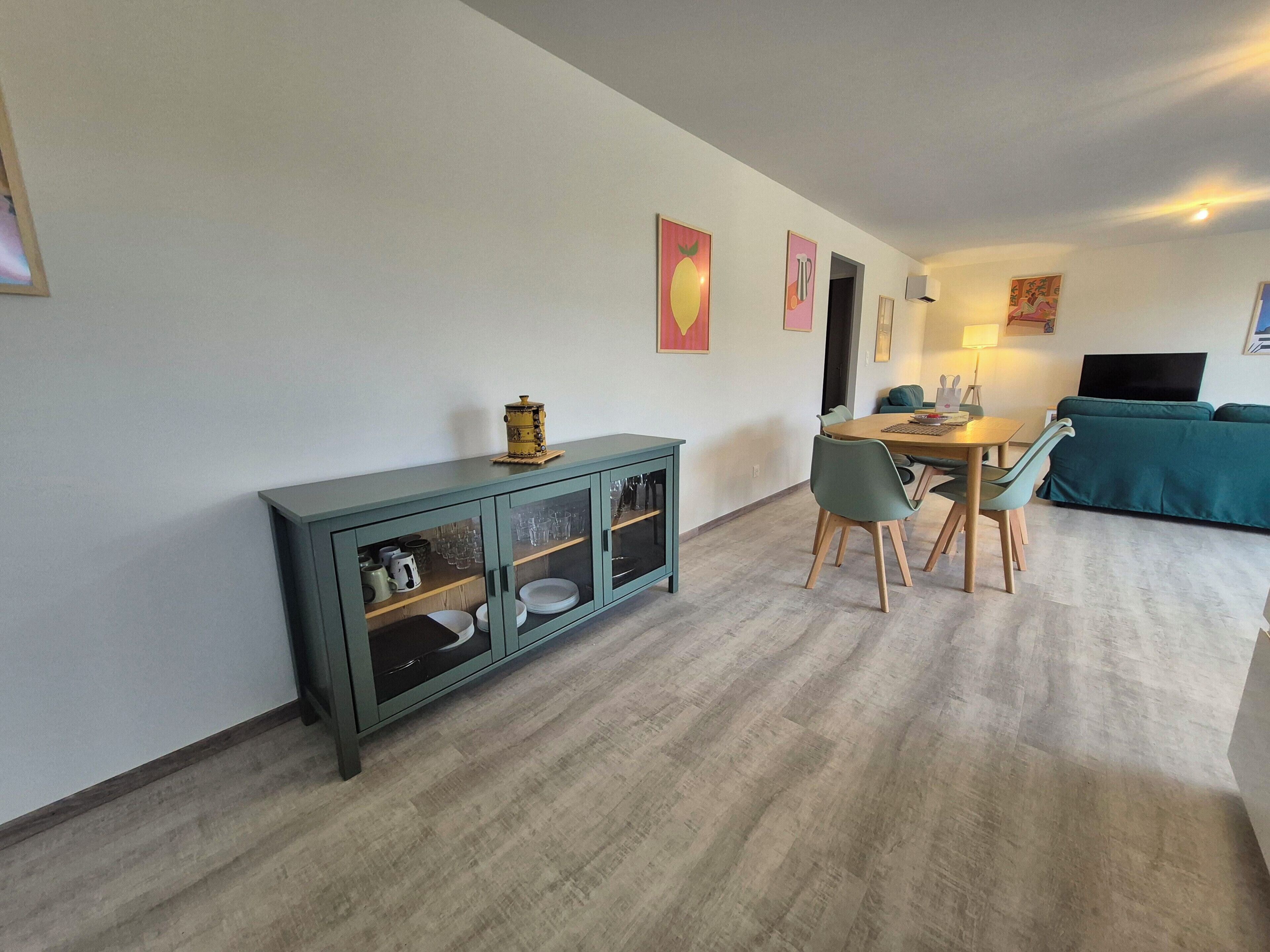 A modern living space with a dining area, a teal cabinet with glass doors, a sofa, and artwork on the walls.