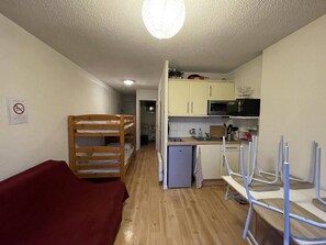 A room with a bunk bed, a small kitchenette, and a red sofa. - Cozy apartment in Barcelonnette - 6 people (Barcelonnette)