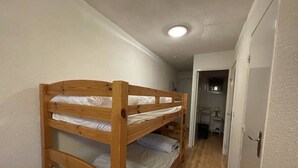 Habitación con literas, cabecero de madera, una puerta blanca y un pasillo que conduce a otra habitación.