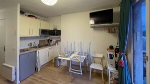 Una cocina compacta con armarios blancos, microondas, lavaplatos y una zona de comedor con sillas blancas.