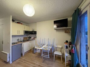 A compact kitchen with white cabinets, a microwave, a sink, and a dining area with white chairs. - Cozy apartment in Barcelonnette - 6 people (Barcelonnette)