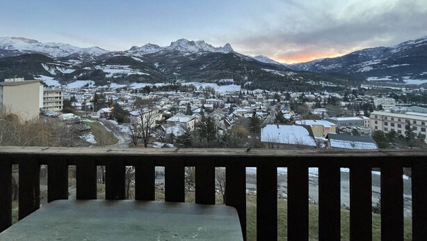 Un pueblo con montañas nevadas al fondo, cielo despejado y vistas desde un balcón.