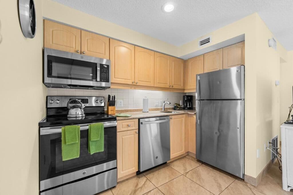 A kitchen with stainless steel appliances, wooden cabinets, a microwave, oven, dishwasher, and a refrigerator.