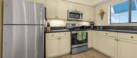 A kitchen with a stainless steel refrigerator, a microwave, an oven, and light-colored cabinets.