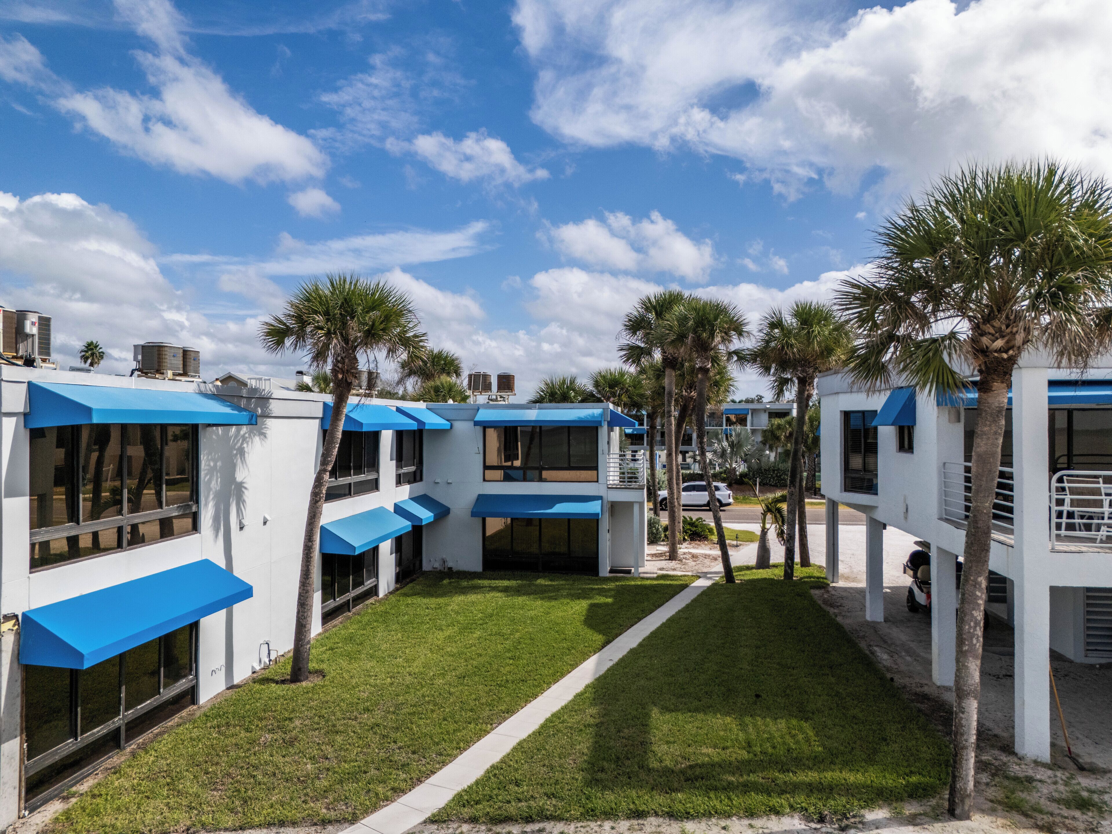 Un hôtel moderne aux façades blanches et bleues, doté d’une pelouse bien entretenue et agrémenté de palmiers.