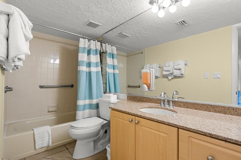 A bathroom with a bathtub, toilet, shower curtain, sink, and mirror.