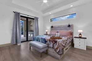 Ein Schlafzimmer mit Bett, Nachttischen, einer Bank, einem Deckenventilator, einem Fenster mit Blick und einer Schiebetür zum Balkon.