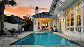 Una piscina con sillas de descanso, un porche cubierto y vistas al atardecer.
