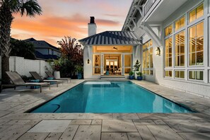 A swimming pool with lounge chairs, a covered patio, and a view of the sunset. - 6BR Coastal Retreat With Golf Cart & Heated Pool! (Panama City Beach)