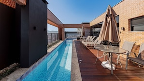 Une piscine sur le toit offrant une vue dégagée sur les gratte-ciel de la ville, entourée de chaises longues et de parasols.