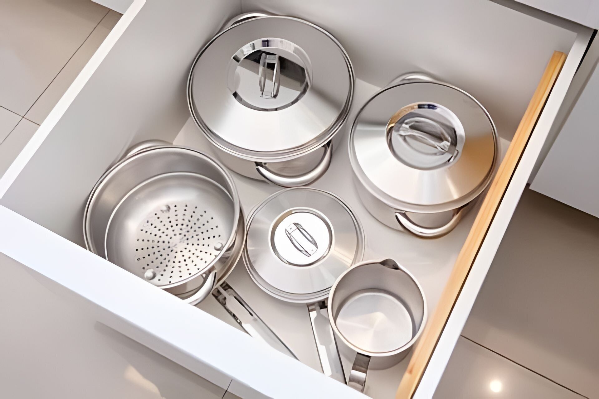 Uma gaveta de cozinha com utensílios de aço inoxidável, incluindo panelas, frigideiras e um escorredor.