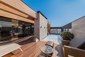 A rooftop with a swimming pool, outdoor seating, and a gym visible through the glass. - Flipchave - Apartamentos Highline design (Joinville)