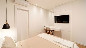 Une chambre à coucher moderne, équipée d’un lit, d’une table de chevet, d’un bureau, d’une chaise et d’un téléviseur fixé au mur.