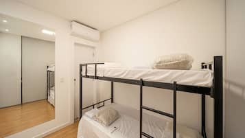 Dormitorio con literas, suelo de madera, espejo y unidad de aire acondicionado.