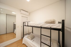 Dormitorio con literas, suelo de madera, espejo y unidad de aire acondicionado.