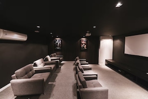 A dark-themed home theater with multiple seating rows, a large screen, and a wall-mounted projector.