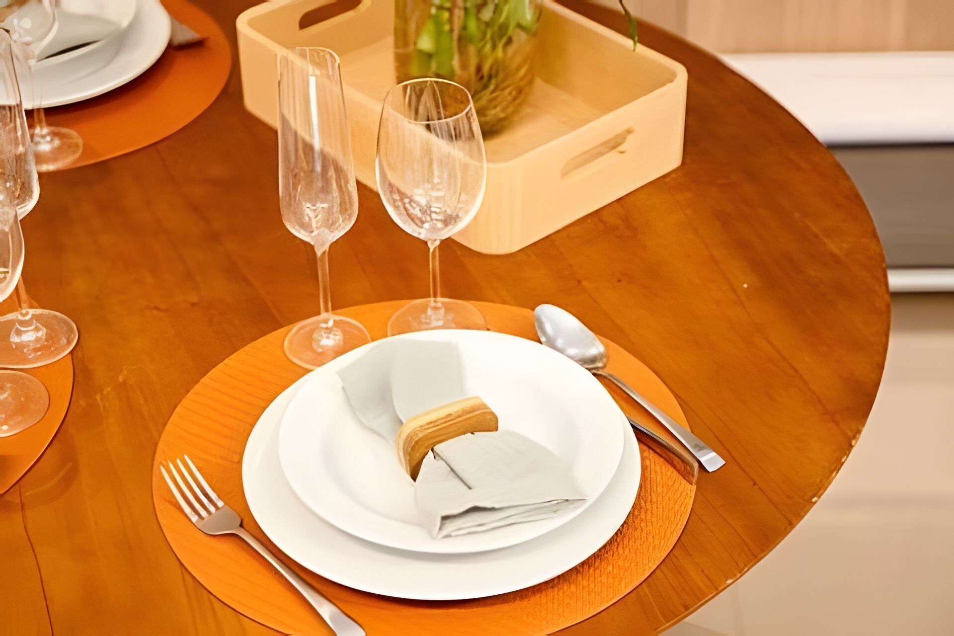 Et spisebord med en hvid tallerken, en serviet, en gaffel, en kniv og to glas.