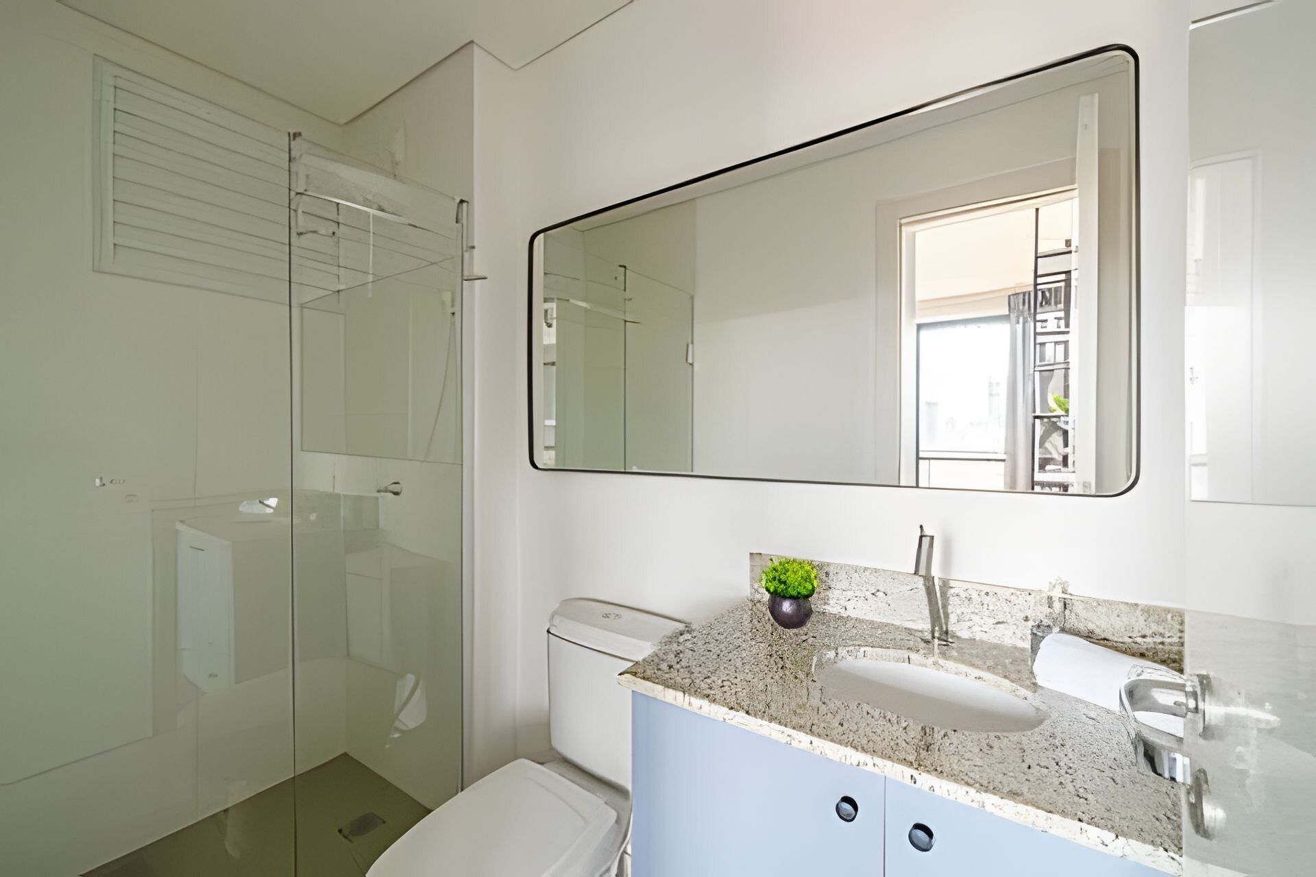 Un baño con cabina de ducha de vidrio, inodoro blanco, lavamanos con encimera de granito y un espejo grande.