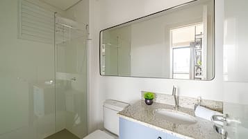Un baño con cabina de ducha de vidrio, inodoro blanco, lavamanos con encimera de granito y un espejo grande.