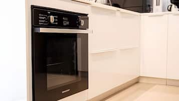 Una cocina con horno integrado, armarios blancos y una encimera.