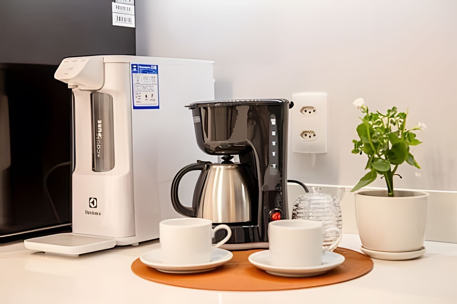 Una cafetera, dos tazas, una planta en maceta y una balanza sobre una mesa.
